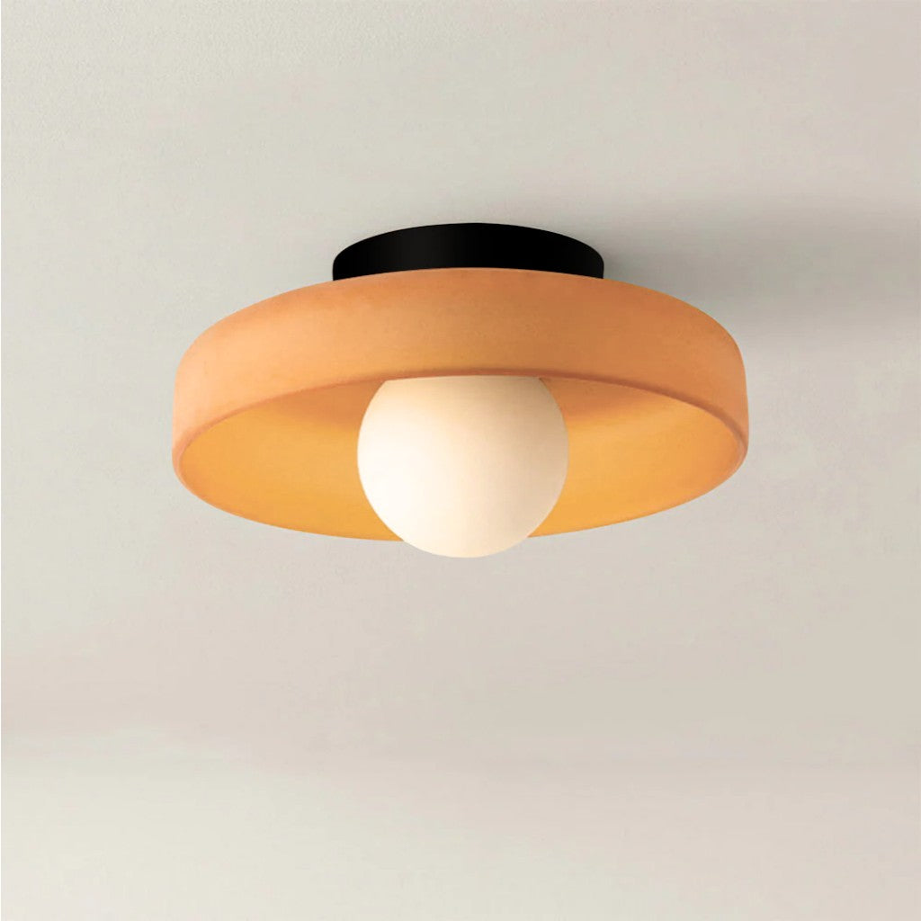 Ceiling light fixture with orange shade and white bulb on a plain background